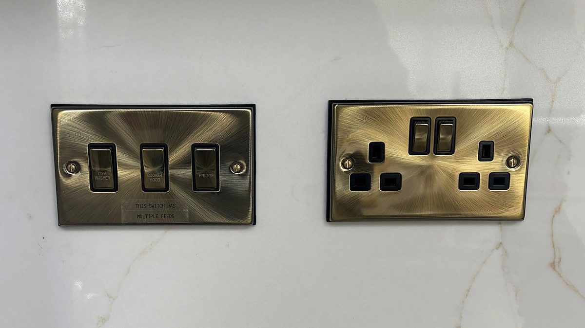 Antique brass 3 gang grid switch and double socket on a white marble splashback